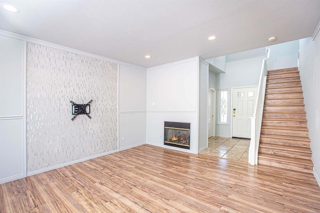 unfurnished living room featuring baseboards, a glass covered fireplace, wood finished floors, stairs, and recessed lighting