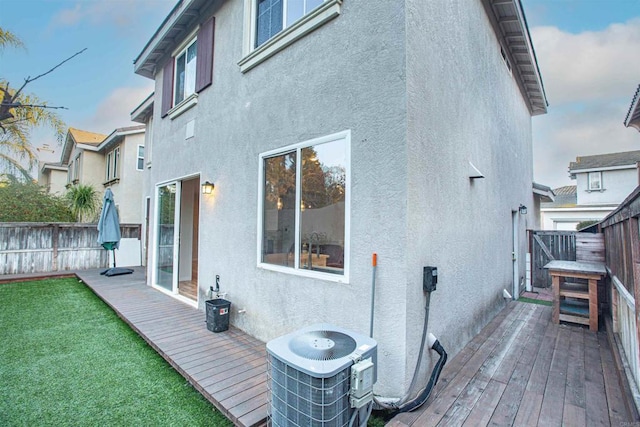 back of property featuring a yard, stucco siding, central AC, fence, and a deck