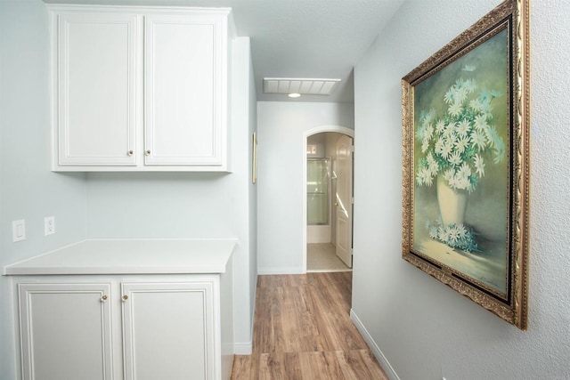 hallway featuring arched walkways, light wood-type flooring, visible vents, and baseboards