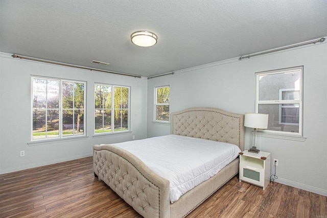 bedroom with baseboards, a textured ceiling, visible vents, and wood finished floors