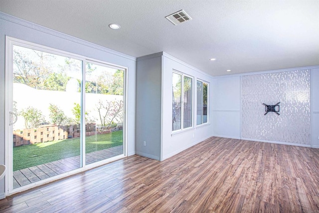 unfurnished room with a wealth of natural light, visible vents, wood finished floors, and ornamental molding