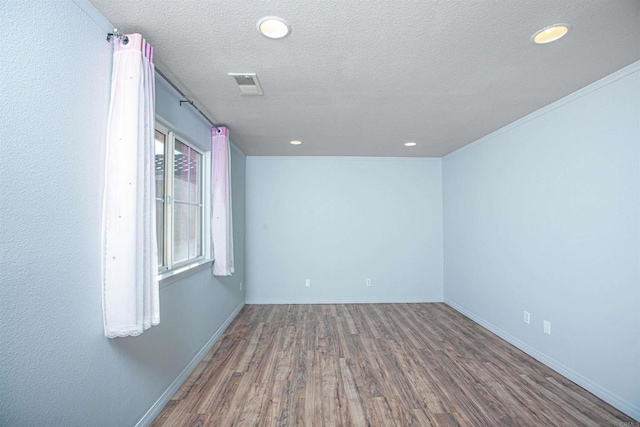 empty room with baseboards, visible vents, wood finished floors, a textured ceiling, and recessed lighting