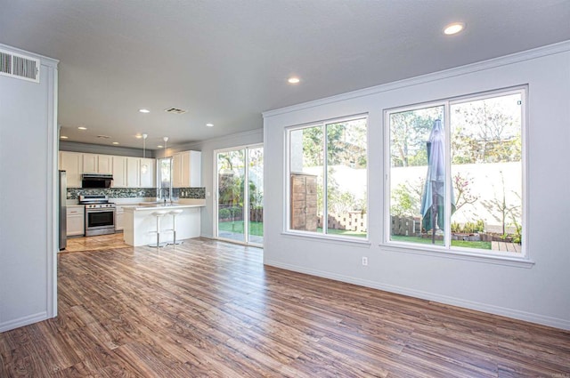 unfurnished living room with ornamental molding, visible vents, baseboards, and wood finished floors