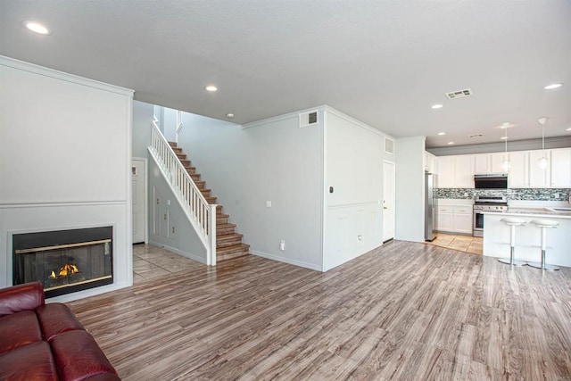 unfurnished living room featuring light wood finished floors, stairway, and visible vents