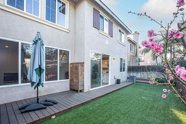 rear view of house with fence, a wooden deck, and stucco siding