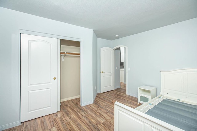 unfurnished bedroom featuring arched walkways, a closet, light wood-style flooring, a textured ceiling, and baseboards