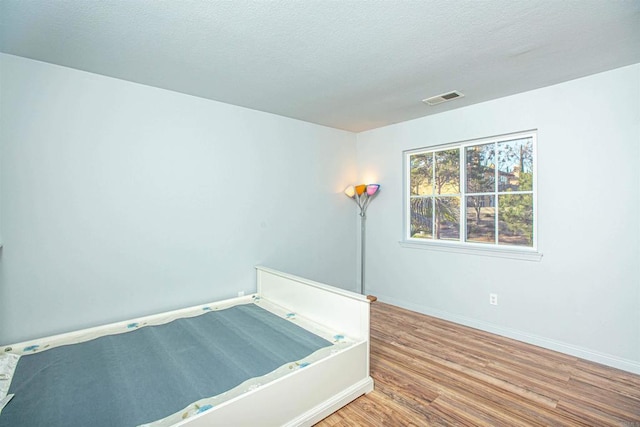 interior space with baseboards, a textured ceiling, visible vents, and wood finished floors