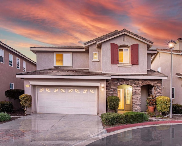 view of front facade featuring an attached garage, concrete driveway, stone siding, a tiled roof, and stucco siding