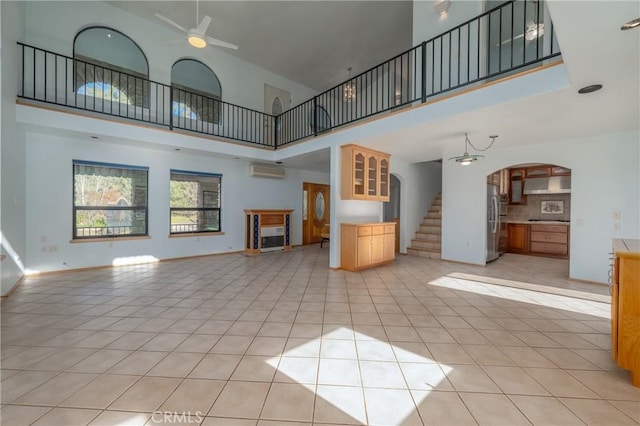 unfurnished living room featuring ceiling fan, a high ceiling, a wall mounted AC, arched walkways, and light tile patterned floors
