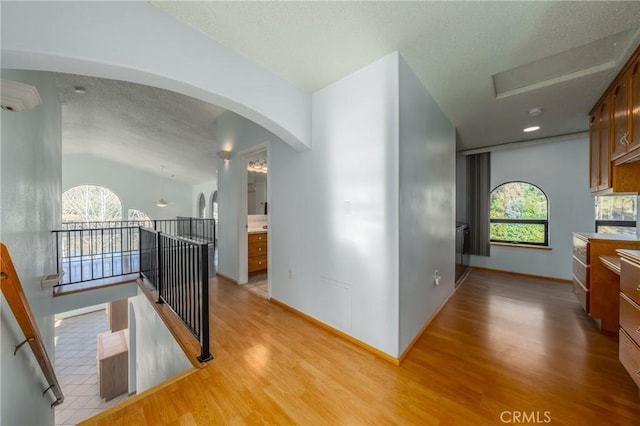 hallway featuring a textured ceiling, baseboards, and light wood-style flooring