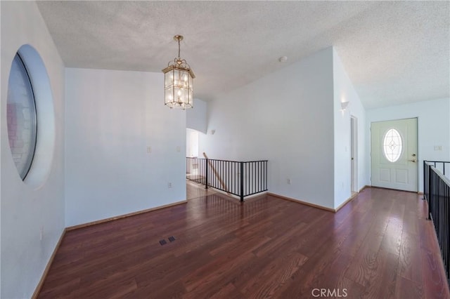 interior space featuring an inviting chandelier, dark hardwood / wood-style flooring, vaulted ceiling, and a textured ceiling