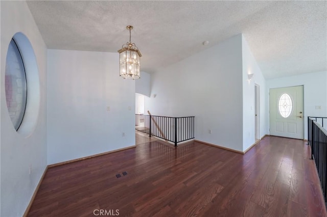 foyer entrance with baseboards, a textured ceiling, wood finished floors, and a notable chandelier
