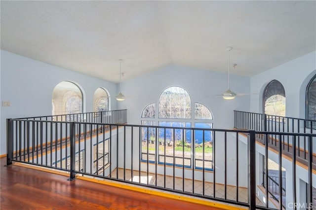 hallway with wood finished floors, vaulted ceiling, and an upstairs landing