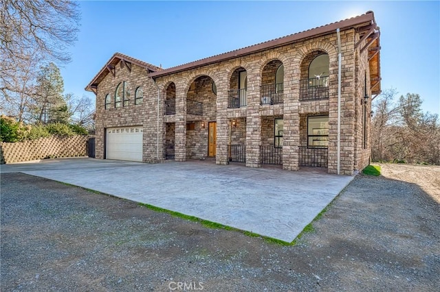 view of front of property with driveway, fence, a balcony, an attached garage, and stone siding