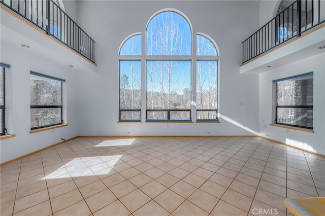 unfurnished living room featuring plenty of natural light, tile patterned floors, baseboards, and a high ceiling