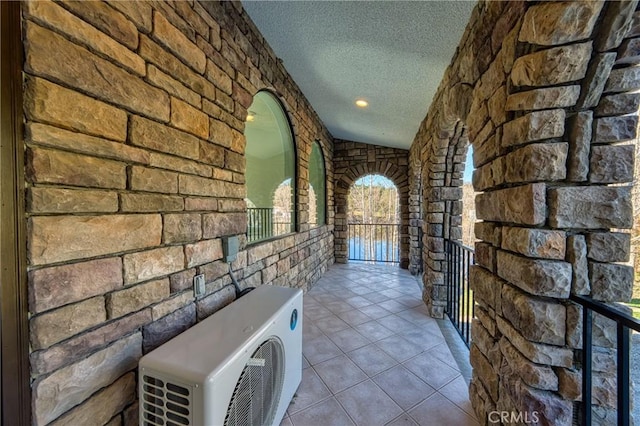 corridor with vaulted ceiling, light tile patterned floors, ac unit, and a textured ceiling