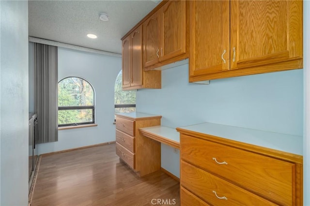 kitchen with light wood-style floors, baseboards, light countertops, built in desk, and brown cabinets