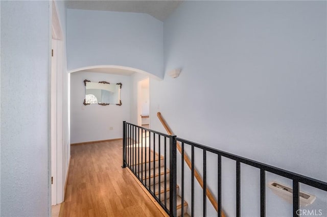 hall featuring high vaulted ceiling, arched walkways, wood finished floors, and an upstairs landing