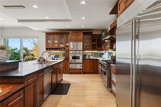 kitchen featuring wall chimney exhaust hood, high quality appliances, sink, and light wood-type flooring