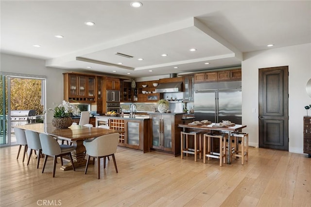 dining room featuring sink, a tray ceiling, and light hardwood / wood-style flooring