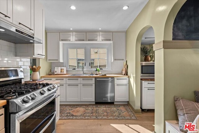 kitchen with appliances with stainless steel finishes, light hardwood / wood-style floors, sink, and butcher block countertops