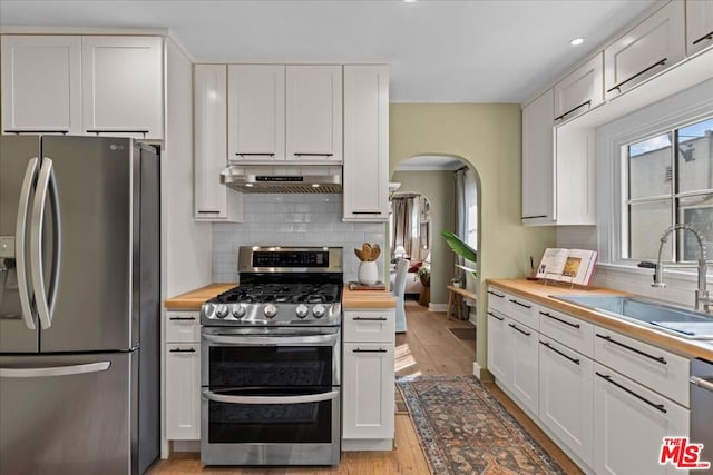 kitchen featuring stainless steel appliances, range hood, butcher block counters, and white cabinets