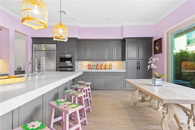 kitchen with gray cabinetry, built in appliances, hanging light fixtures, ornamental molding, and decorative backsplash