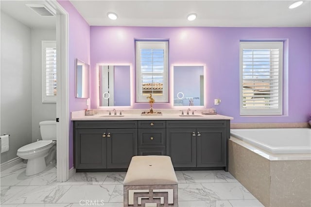 bathroom featuring vanity, a relaxing tiled tub, and toilet