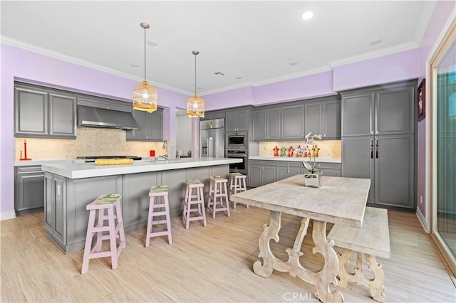 kitchen featuring appliances with stainless steel finishes, gray cabinetry, hanging light fixtures, an island with sink, and wall chimney exhaust hood