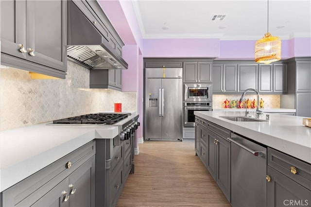 kitchen with sink, built in appliances, decorative light fixtures, ornamental molding, and wall chimney range hood