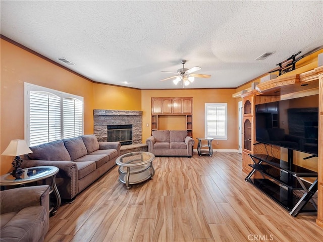 living room with a fireplace, ceiling fan, crown molding, a textured ceiling, and light hardwood / wood-style flooring