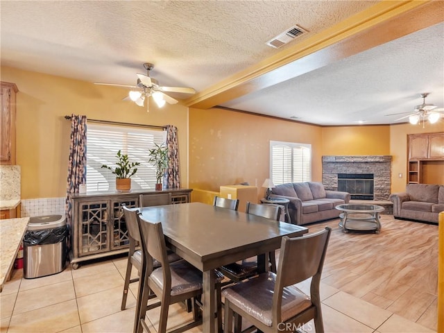 dining space with light tile patterned flooring, a textured ceiling, a fireplace, and ceiling fan