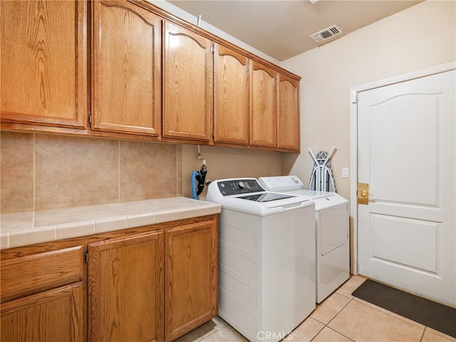 laundry area with light tile patterned floors, washer and clothes dryer, and cabinets