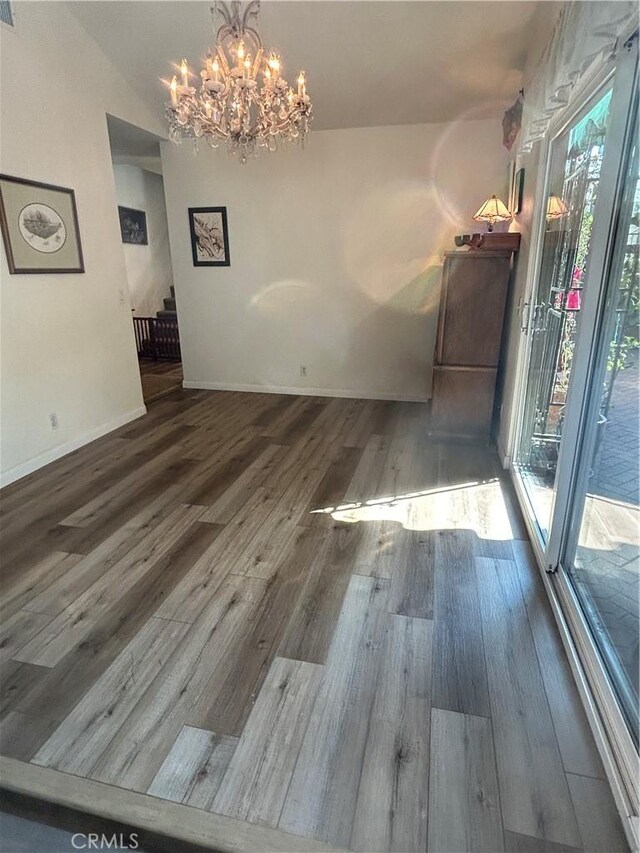 unfurnished dining area with a notable chandelier, wood-type flooring, and vaulted ceiling