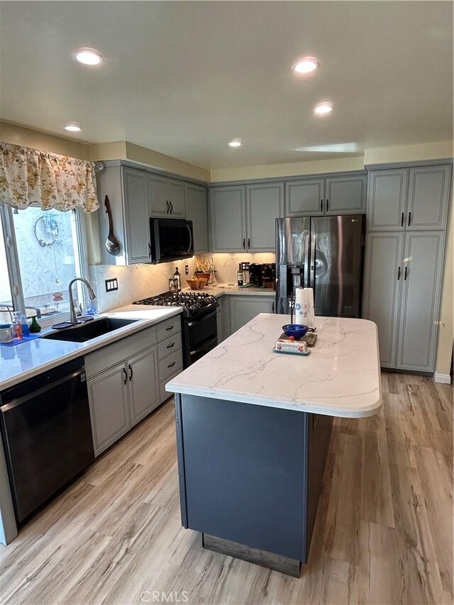 kitchen with sink, gray cabinets, a kitchen island, light stone countertops, and black appliances