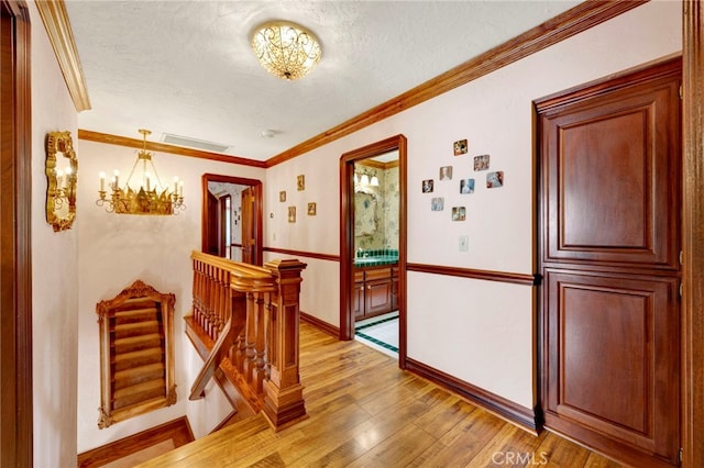 corridor featuring an inviting chandelier, crown molding, a textured ceiling, and light wood-type flooring