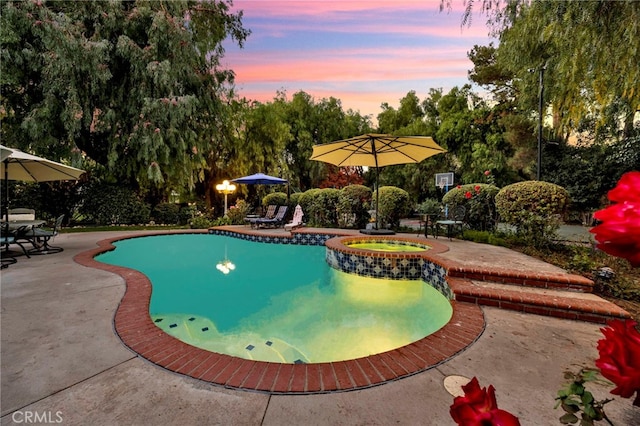 pool at dusk featuring a patio area and an in ground hot tub