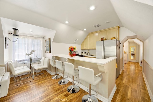 kitchen featuring light hardwood / wood-style flooring, stainless steel fridge, a kitchen breakfast bar, vaulted ceiling, and kitchen peninsula