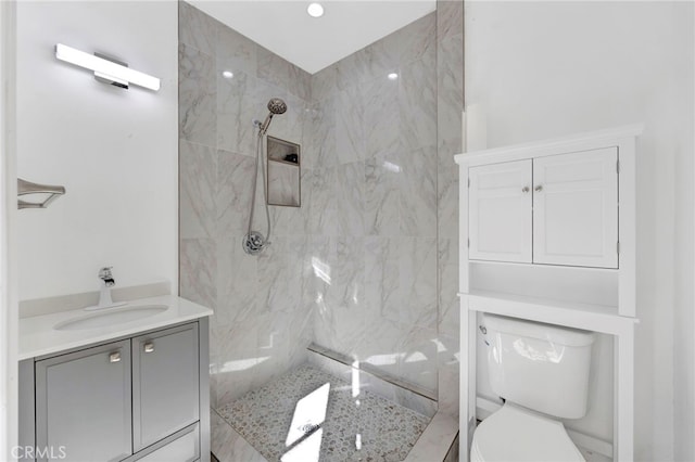 bathroom with a tile shower, vanity, and toilet