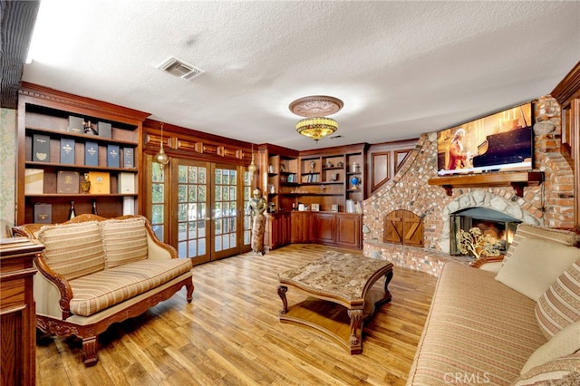 sitting room featuring light wood-type flooring, a textured ceiling, a fireplace, and french doors