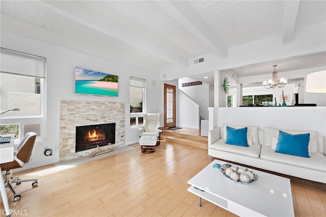 living room featuring a stone fireplace, hardwood / wood-style floors, a notable chandelier, and beam ceiling