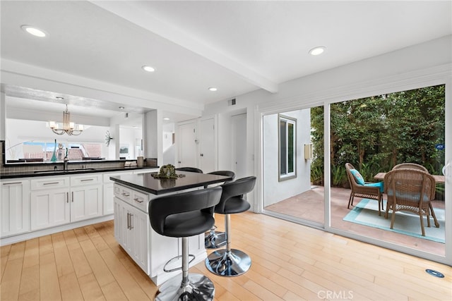 kitchen featuring a kitchen island, beamed ceiling, white cabinetry, sink, and hanging light fixtures