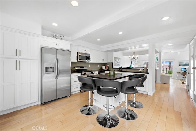 kitchen with a breakfast bar area, hanging light fixtures, stainless steel appliances, white cabinets, and beamed ceiling