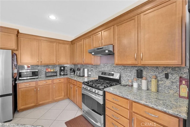 kitchen with tasteful backsplash, appliances with stainless steel finishes, light stone countertops, and light tile patterned floors