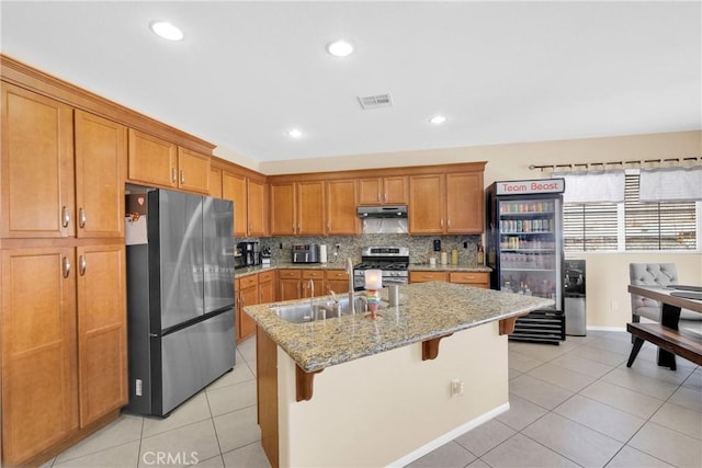 kitchen with light stone counters, tasteful backsplash, a kitchen breakfast bar, an island with sink, and stainless steel appliances