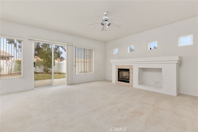 unfurnished living room featuring a tiled fireplace, light colored carpet, and ceiling fan