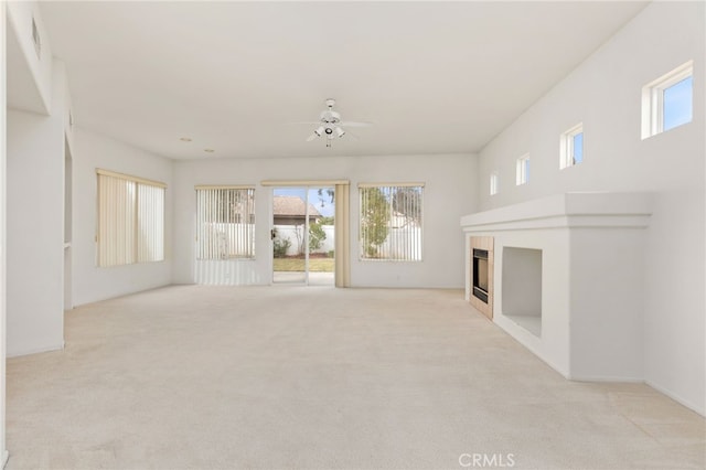 unfurnished living room with a fireplace, light colored carpet, and ceiling fan