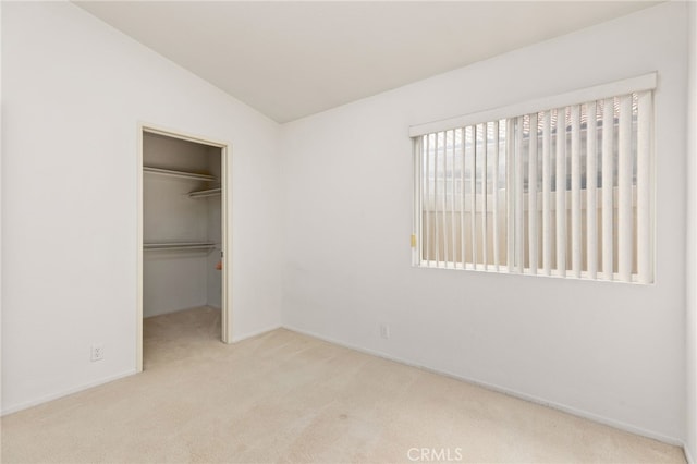 unfurnished bedroom featuring a spacious closet, vaulted ceiling, light colored carpet, and a closet