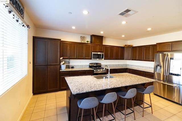 kitchen featuring light tile patterned flooring, stainless steel appliances, a kitchen island with sink, and a breakfast bar area