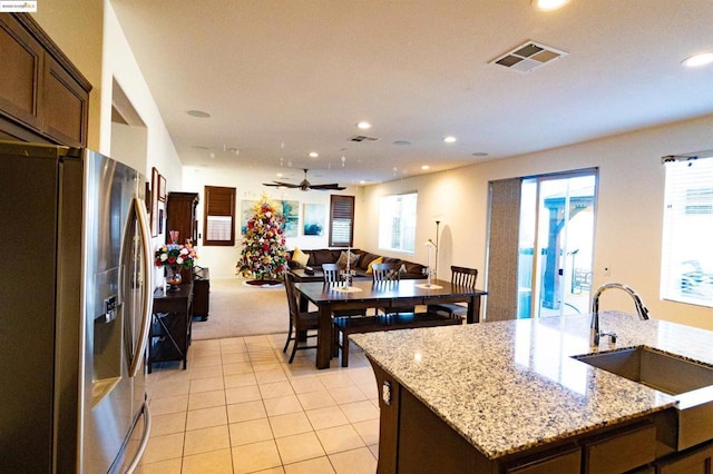 kitchen featuring stainless steel refrigerator with ice dispenser, sink, a center island with sink, light tile patterned floors, and light stone countertops